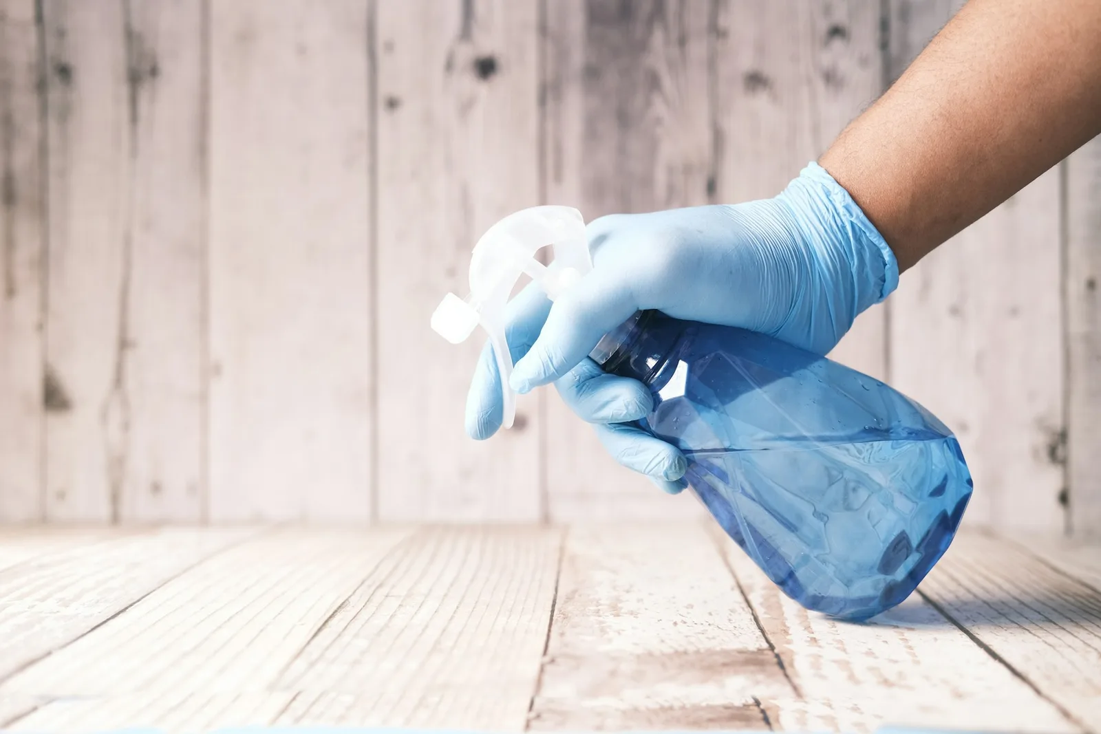 Gloved hand holding a blue spray bottle over a wooden surface, illustrating what you should not clean with hydrogen peroxide on delicate or damage-prone materials. Image by Towfiqu barbhuiya www.unsplash.com