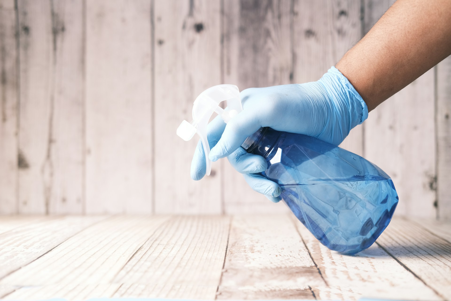 what-you-should-not-clean-with-hydrogen-peroxide Gloved hand holding a blue spray bottle over a wooden surface, illustrating what you should not clean with hydrogen peroxide on delicate or damage-prone materials. Image by Towfiqu barbhuiya www.unsplash.com